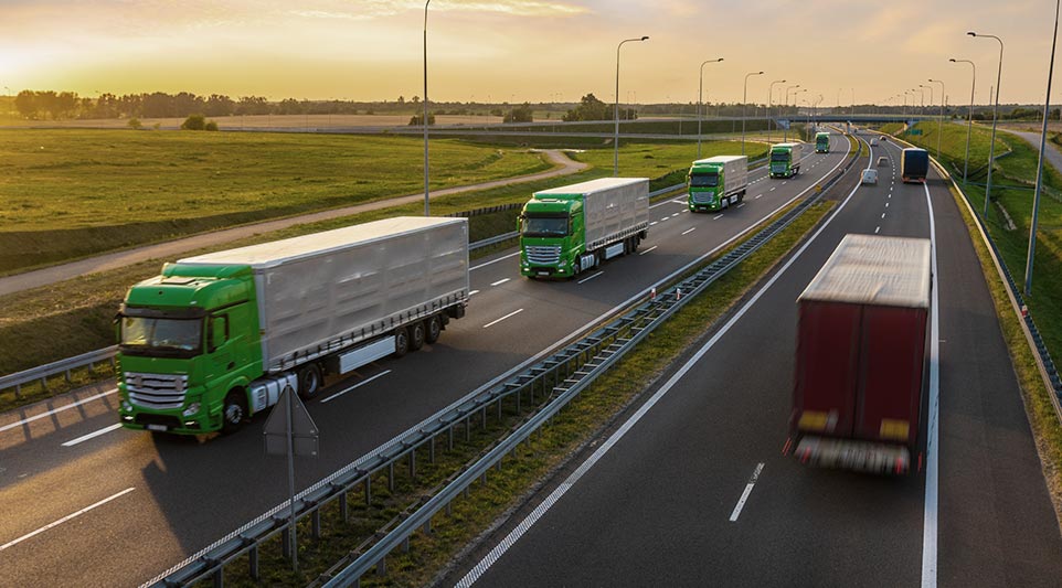 Kolumna zestawów ciężarowych na autostradzie o zachodzie słońca
